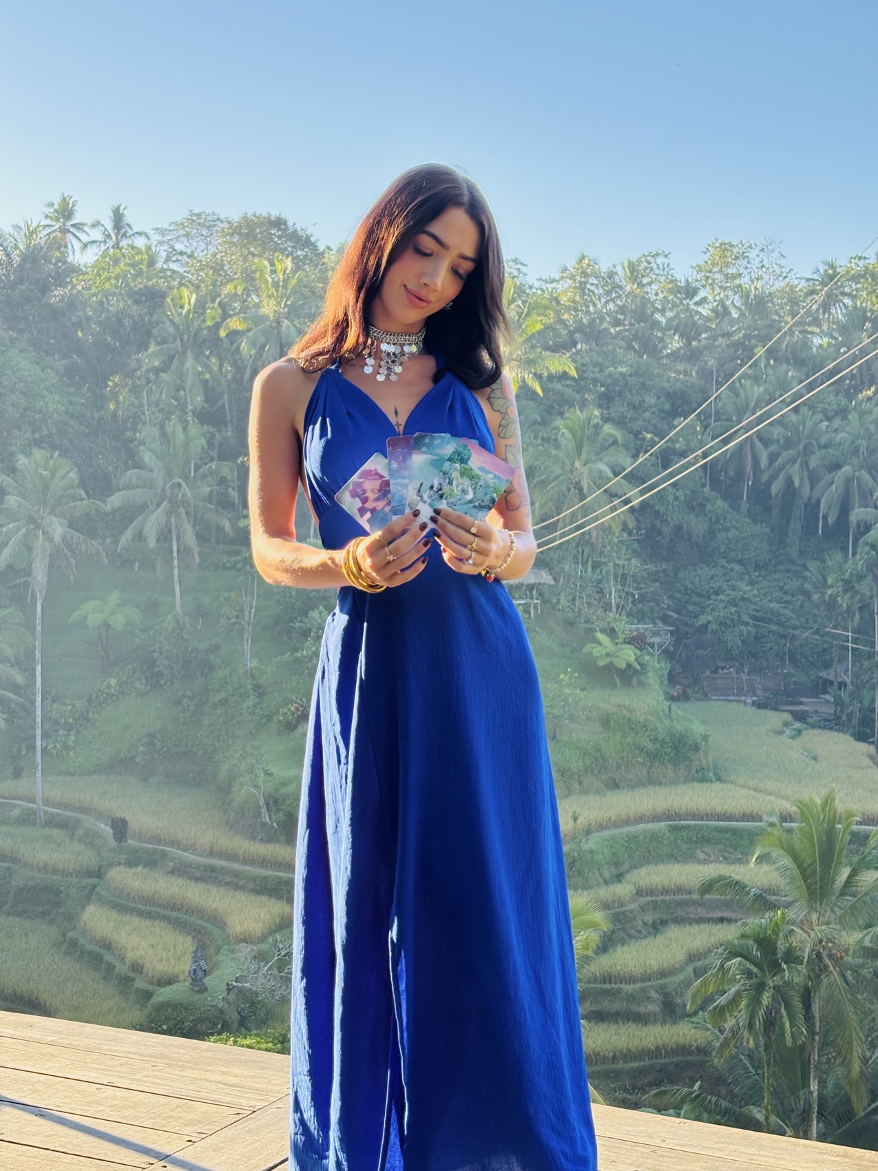 MAÏA in a blue gown holding tarot cards above the Ubud rice terraces
